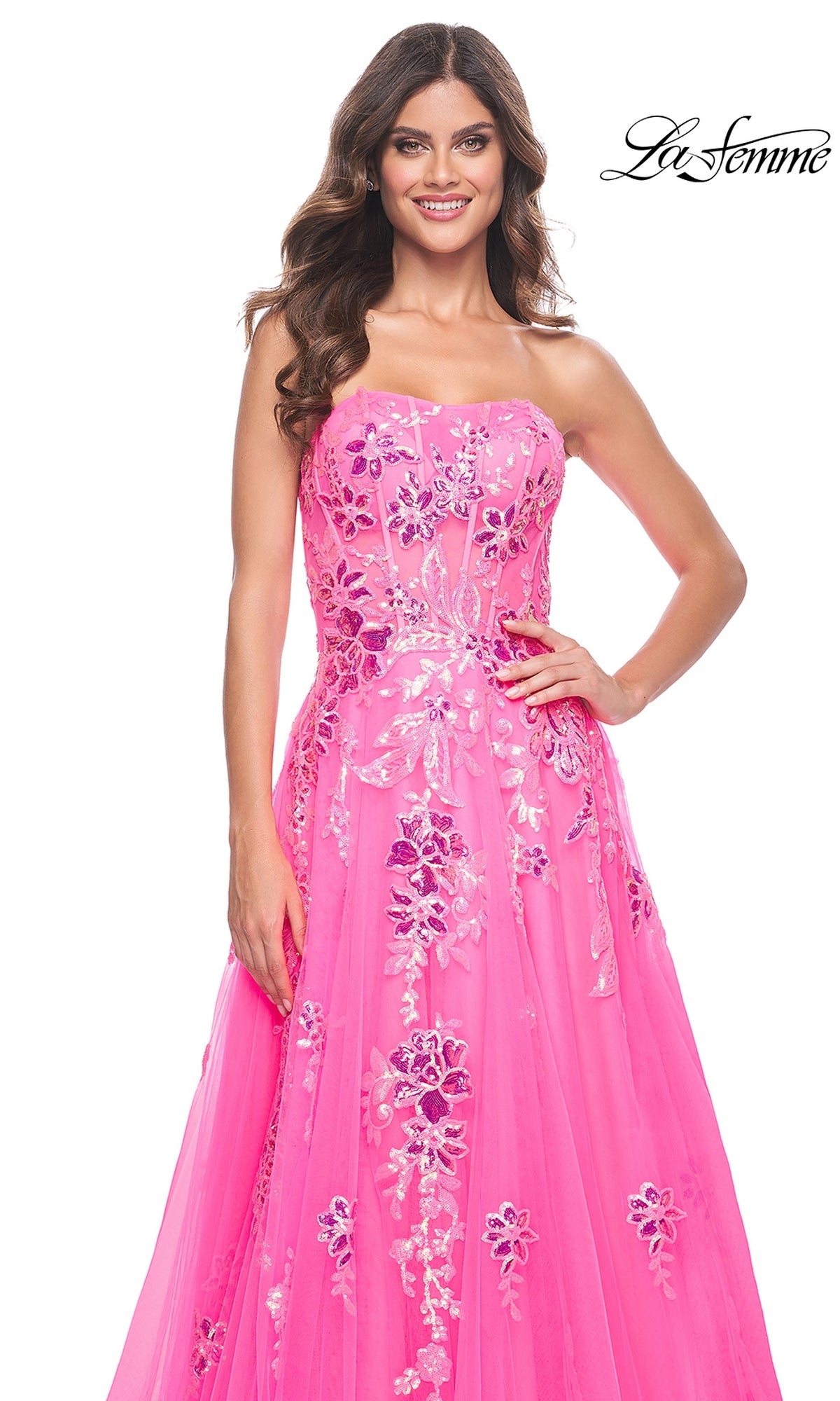 A woman poses with one hand on her hip, wearing the La Femme Neon Pink Long Prom Ball Gown 32137— a strapless style featuring sequin floral embellishments. The